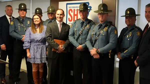 Sarah Huckabee Sanders re-wearing a ruffled blue striped dress next to Arkansas state police