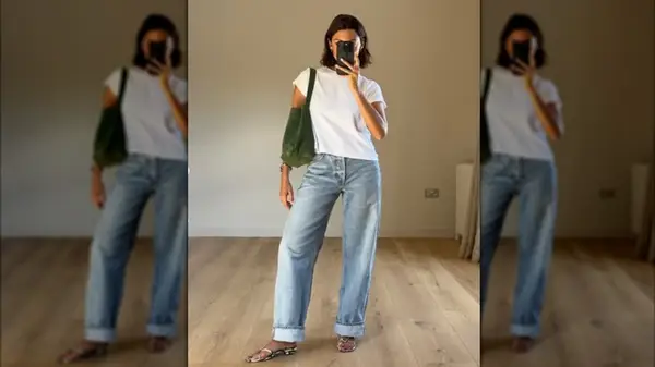 A woman photographing herself in the mirror wearing jeans, a white tea, and strappy sandals