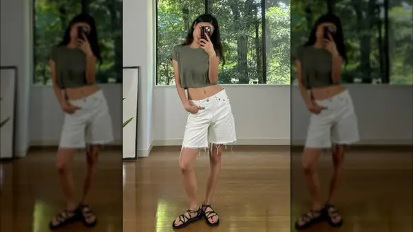 A woman photographing herself in a mirror wearing white cutoff shorts
