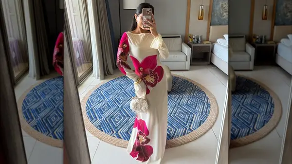 Woman taking a mirror selfie while wearing a cream dress featuring large flowers