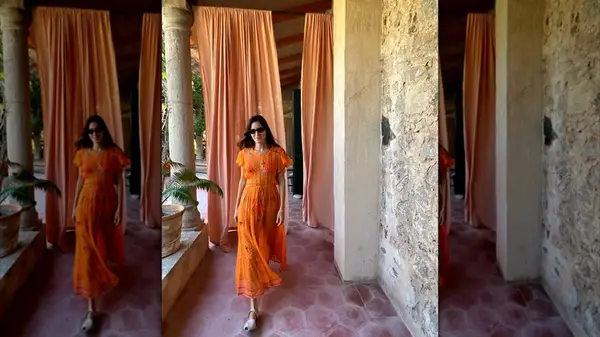 Woman wearing a sheer orange gown while walking an outdoor corridor