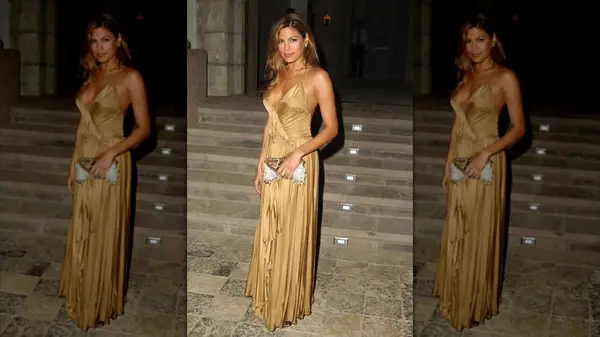 Eva Mendes pising in front of stone steps while wearing a golden gown