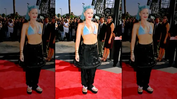 Gwen Stefani on the red carpet with blue hair, a blue bikini top and a skirt and pants