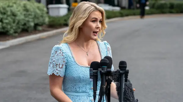 Karoline Leavitt in a blue lace dress behind a podium in April 2025