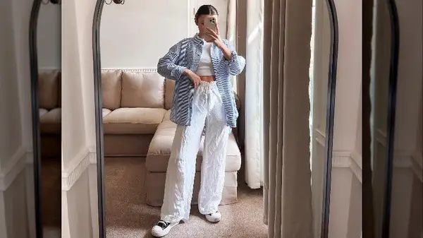 Woman taking mirror selfie in white outfit with blue button-down