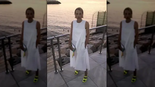 A woman standing next to the water wearing a white dress and neon yellow sandals