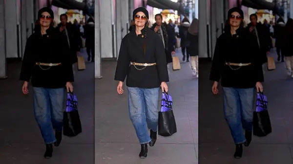 Katie Holmes walking outside in jeans and a black jacket with a hat