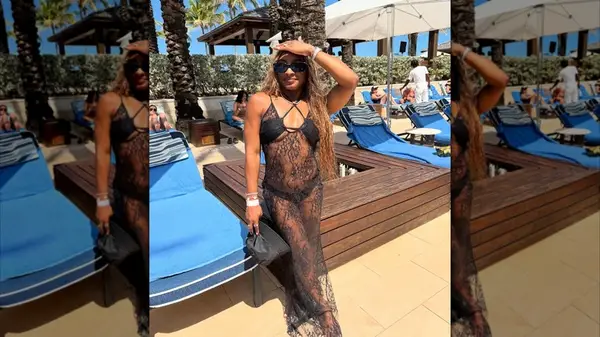 Simone Biles posing in front of lounge chairs while wearing a black bikini and lace cover-up