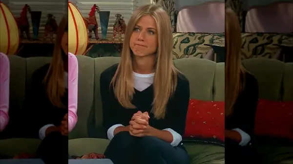 Rachel Green sitting on a couch in a black sweater layered over a long-sleeve white tee