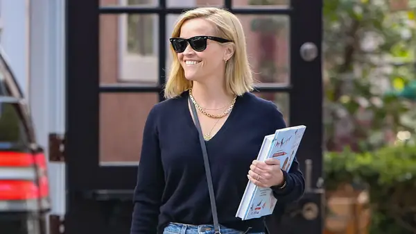 Reese Witherspoon walking with a book wearing sunglasses