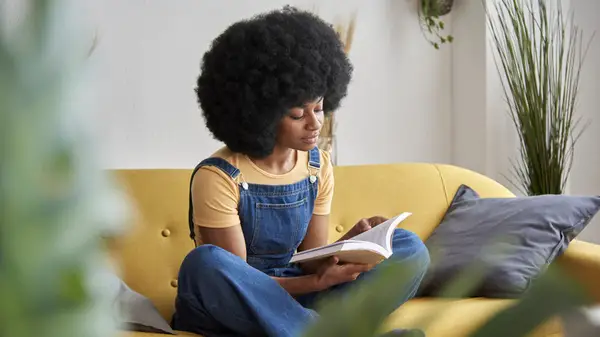 A woman sits on a sofa and reads a book