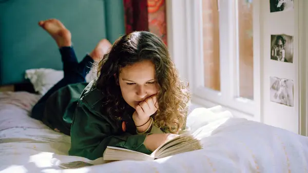 A woman lies on her bed and reads a book