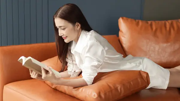 Woman lies comfortably on her couch and reads a book