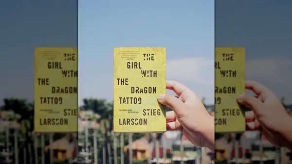 A hand holding a copy of the novel 