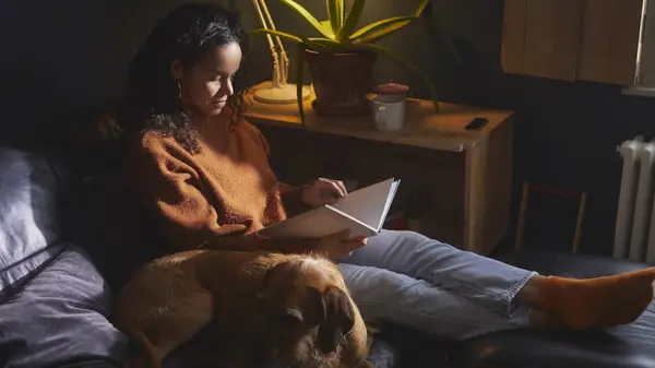 Woman reading book on the couch with her dog
