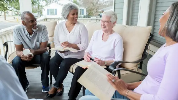 A group of older men and women sitting on a porch, holding open books