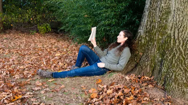 Woman reading a book outside in the fall leaves
