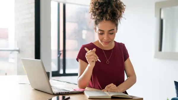 Person writing in journal beside laptop