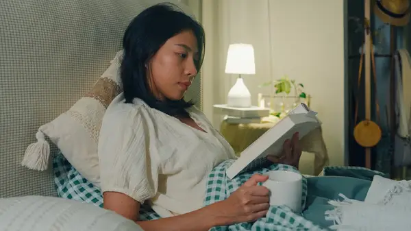 A young woman in bed with a book