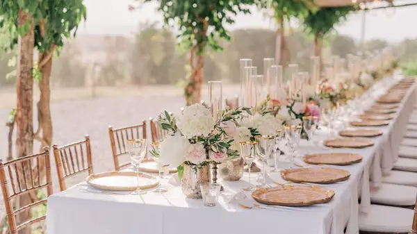 Tables topped with a white table cloth, floral center pieces, candles, glasses and other tableware