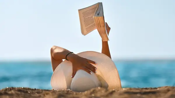 Woman in a sunhat reading on beach