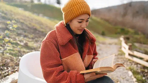 Cozy-looking woman reading a book outside