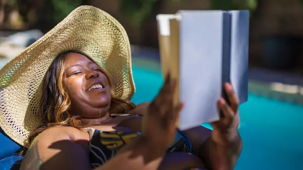 A woman reading on the beach wearing an orange bathing suit next to an inflatable swimming toy