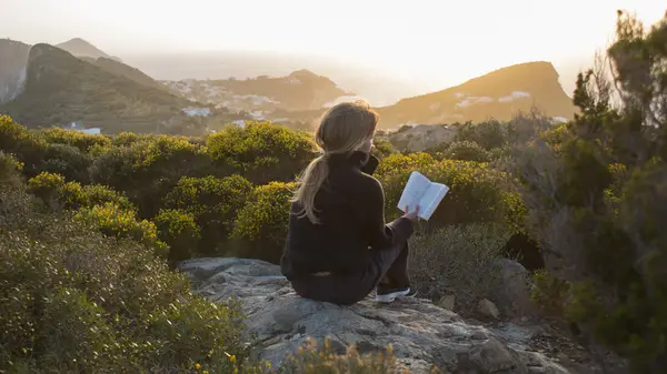 A woman sits on a rock and reads a book