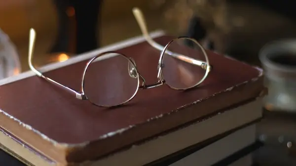 A stack of old books with glasses on top of them and a cup of tea in the background