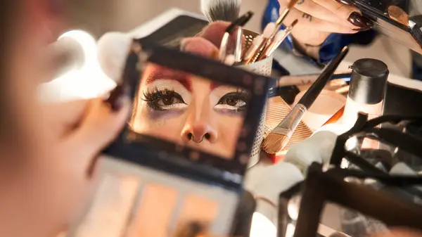 Drag queen applying makeup in mirror