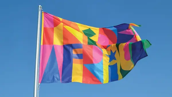 Colorful flag on a flag pole billows in the wind against a blue sky