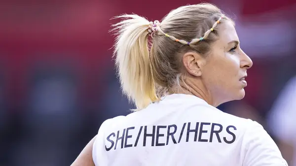 A woman wearing a she/her top, looking away