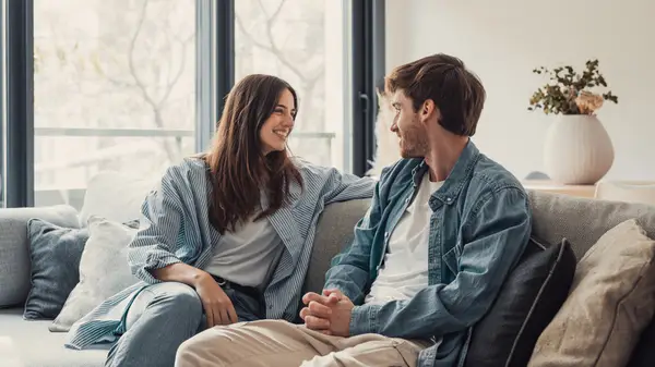 A couple sitting on the couch, talking and smiling