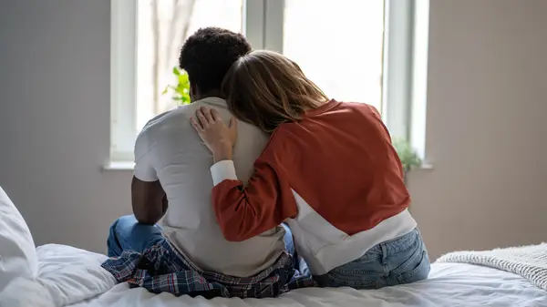 A couple sitting on a bed with their backs to the camera