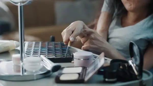 Disabled woman holding makeup brush to apply makeup from palettes on a table
