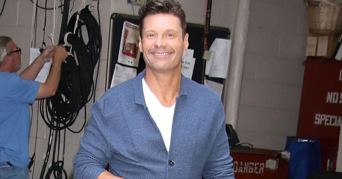 Ryan Seacrest stoi w niebieskim garniturze i uśmiecha się