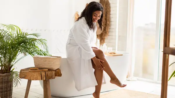 smiling woman in bathrobe sitting next to bathtub