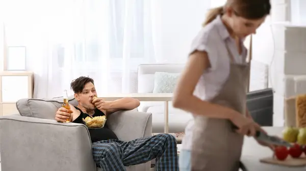 woman cooking while boyfriend lounges