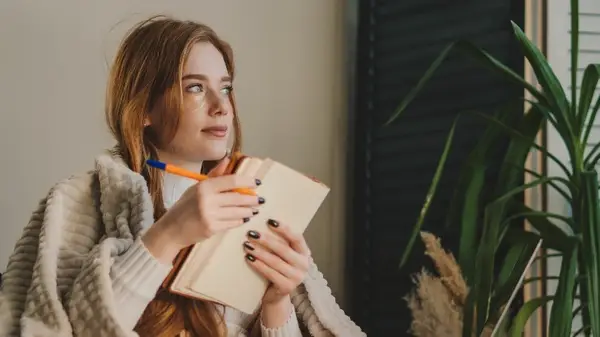 Woman holding journal, looking out of window