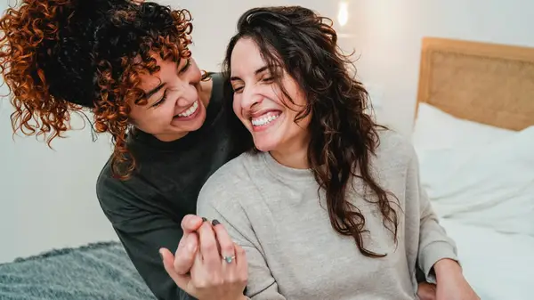 Couple happy and laughing on a bed while holding hands