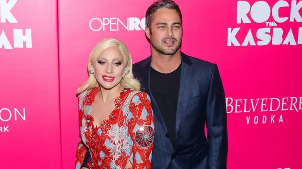 Lady Gaga in a red dress with Taylor Kinney in a blue suit at an event