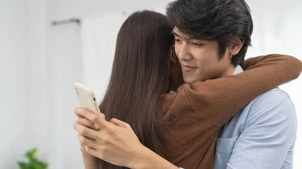 man sends text message while hugging partner