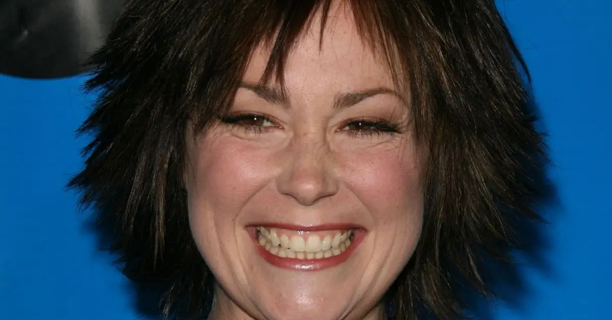 Kim Rhodes mit braunen Haaren lächelt vor blauem Hintergrund