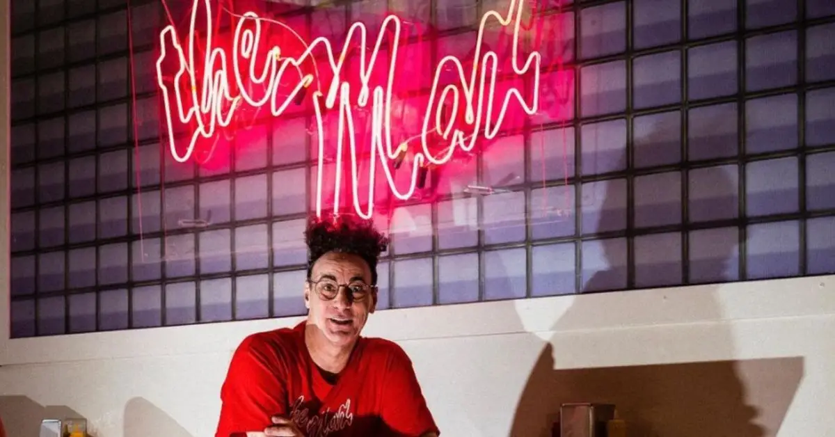 Ed Alonzo sentado em um restaurante com o logotipo do The Max