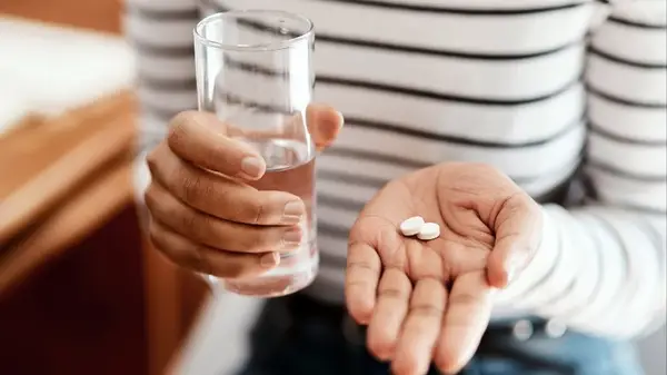 Woman holding two medication tablets with water