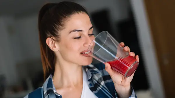 Woman drinks glass of dark red juice