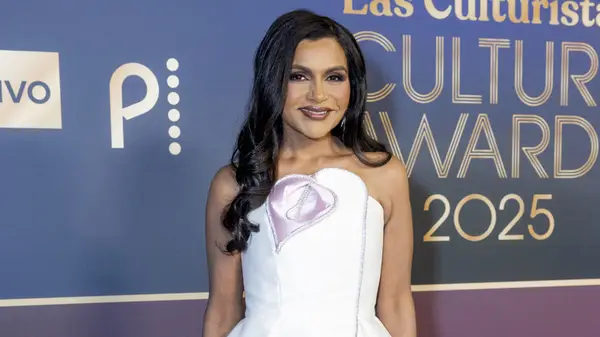 A medium shot of Mindy Kaling on the red carpet, wearing a light pink, fitted dress
