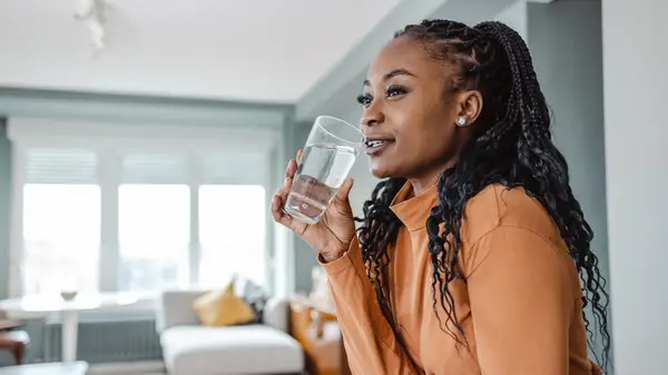 Woman in kitchen drinks a glass of water