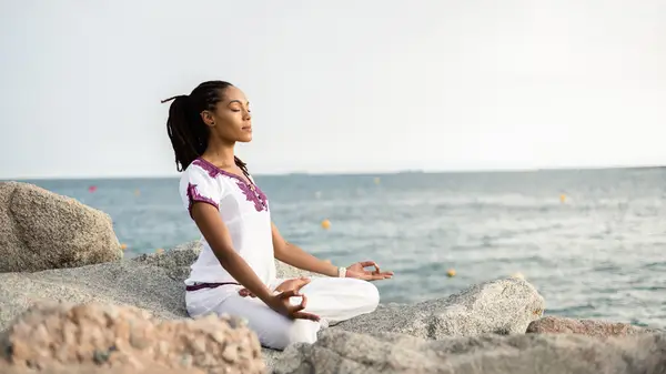 Woman meditating on rocks near water