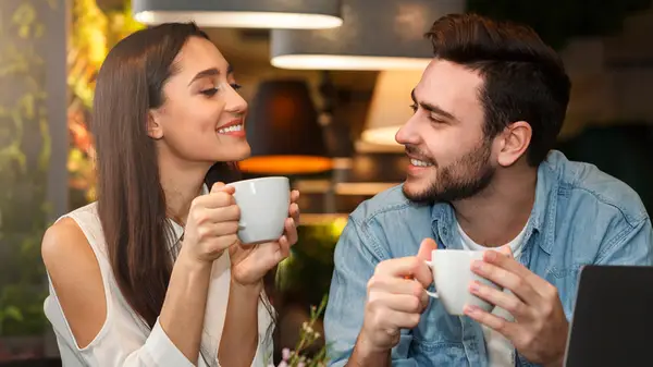 Couple on a date, both smiling, holding mugs